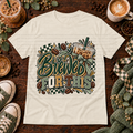 Cream graphic T-shirt with iced coffee, coffee beans, bows, and the phrase Brewed for This