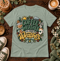 Sage green graphic T-shirt with hot and iced coffee, seasonal weather icons, bows, and the phrase Coffee Weather Is Every Weather