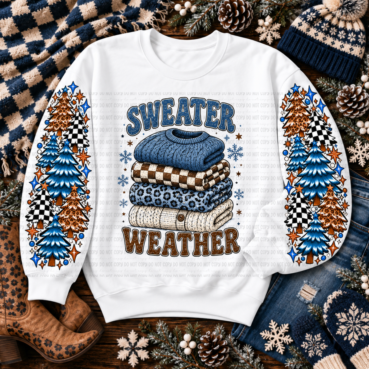 White sweatshirt with stacked sweaters, colorful evergreen trees, snowflakes, stars, and Sweater Weather lettering
