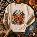 Cream crewneck sweatshirt with an orange butterfly, floral graphics, and Wildly Becoming lettering